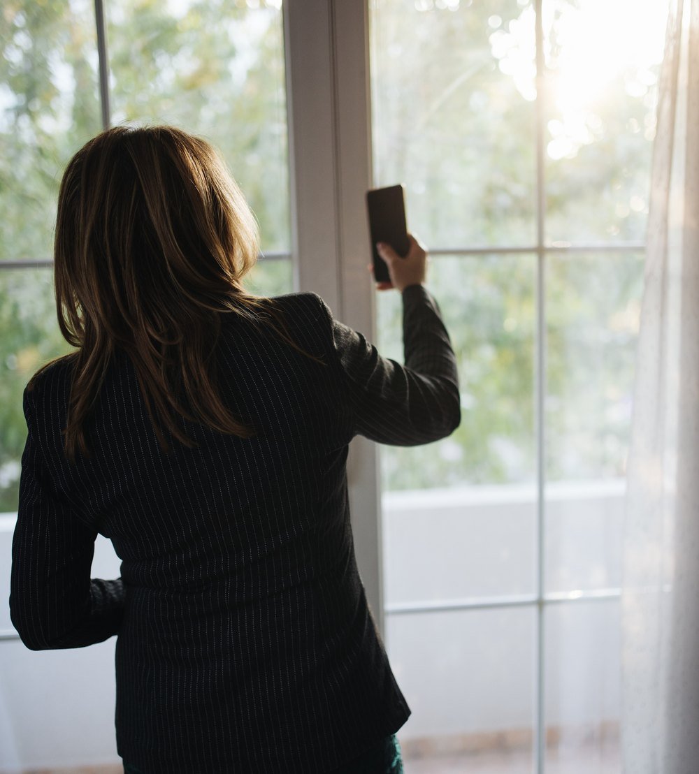 A person standing at a window holding a phone
