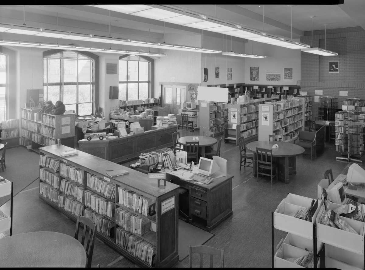 A public library reference room with a Readers Reference desk, shelves of books and early desktop computers.