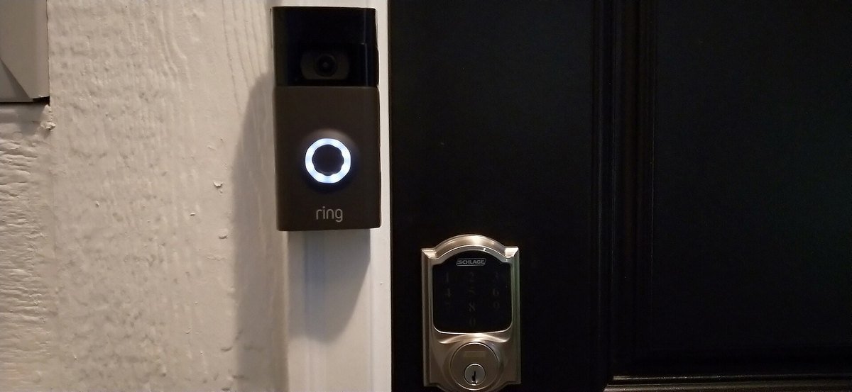 A Ring video doorbell mounted beside a front door next to a smart lock