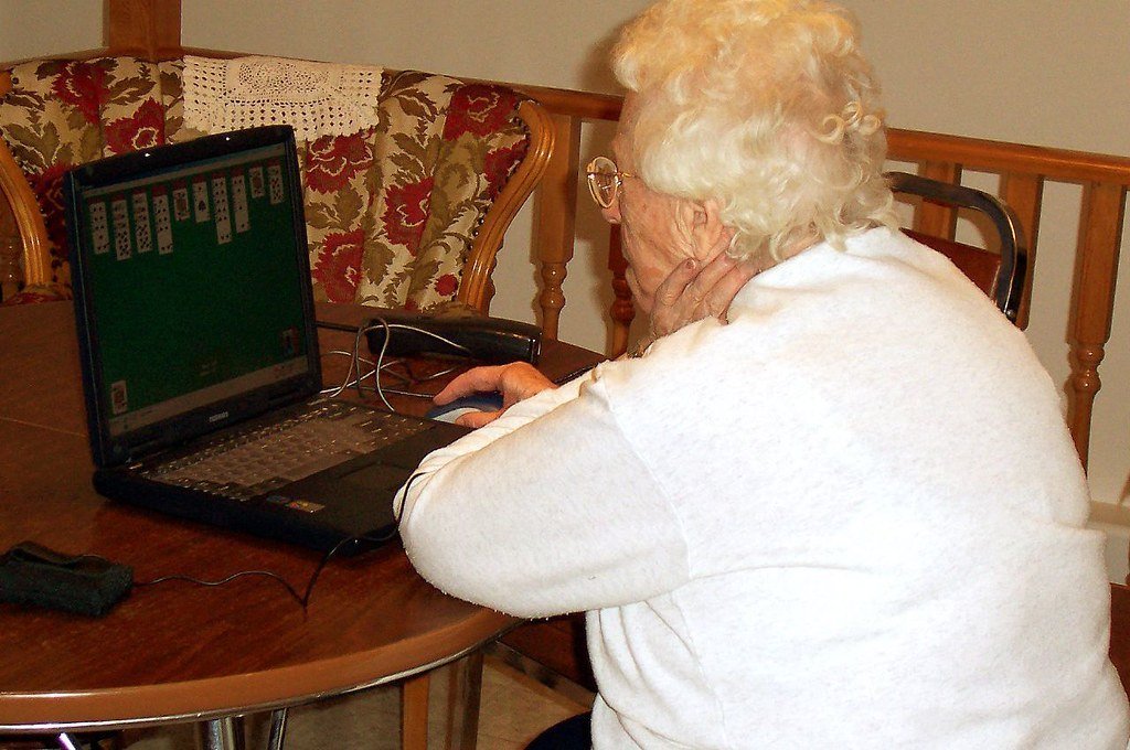An older woman sitting at a kitchen table using a laptop computer