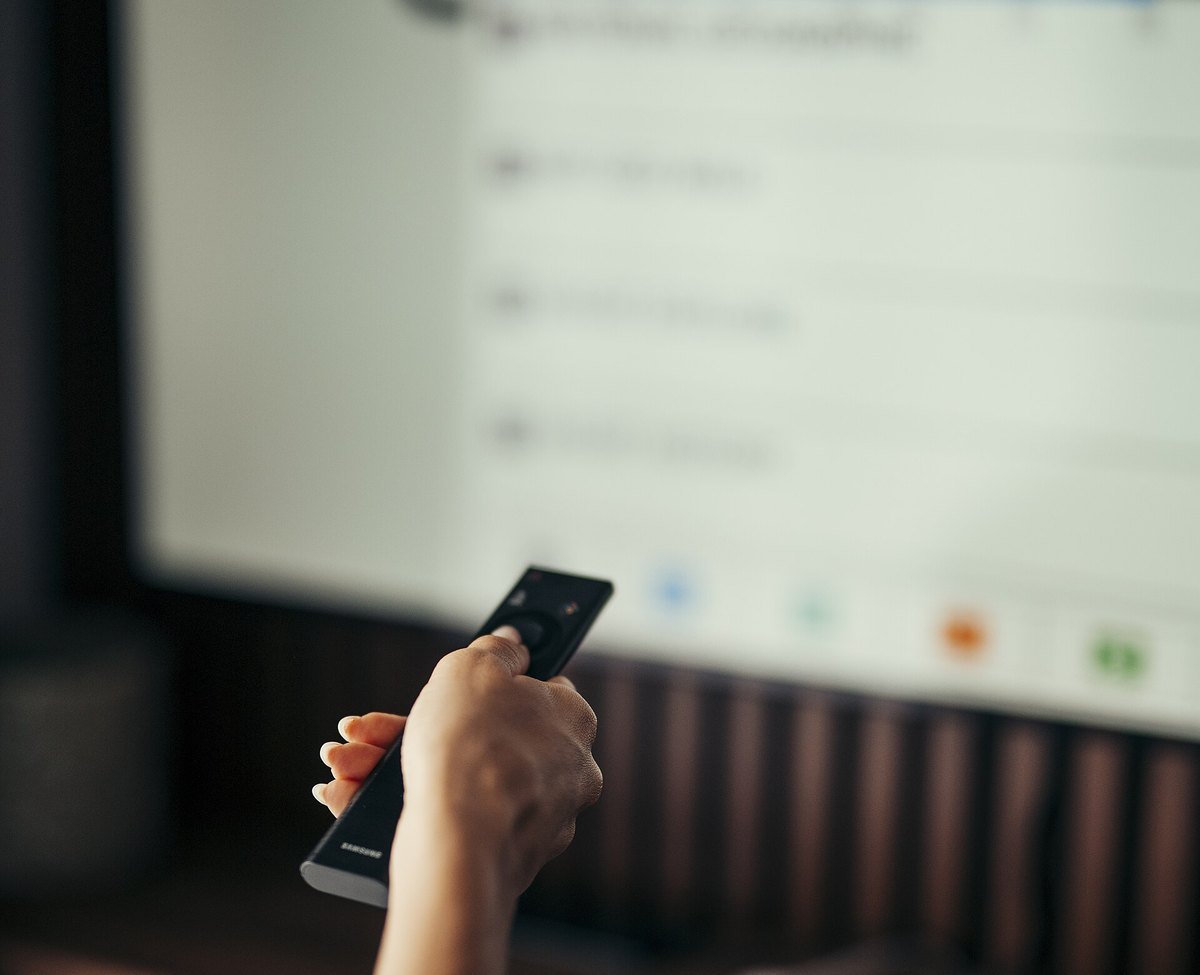 A person pointing a remote control at a television showing an on-screen settings list