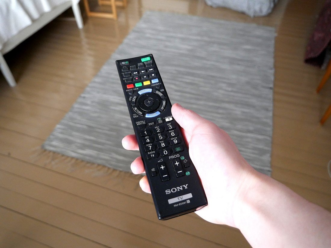 A hand holding a Sony television remote control in a living room