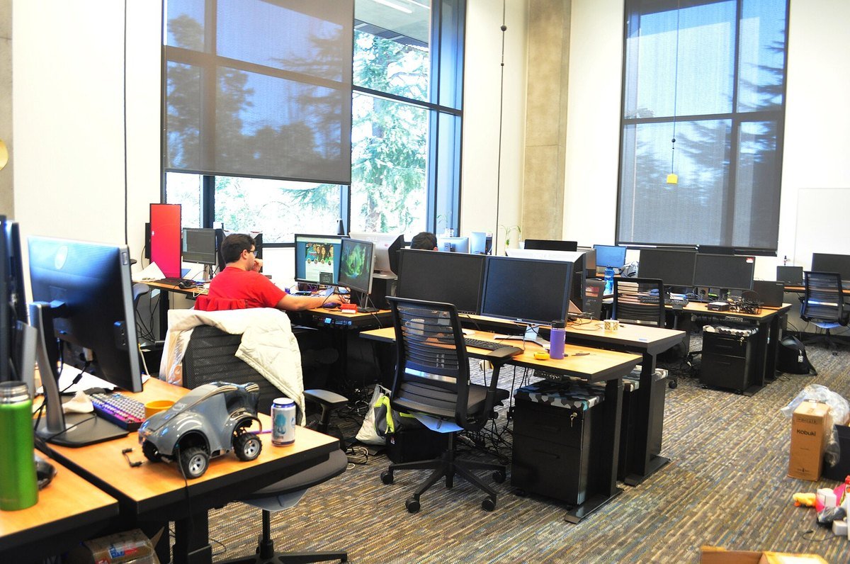 A university robotics research lab with rows of desks, monitors and a small wheeled robot on a desktop
