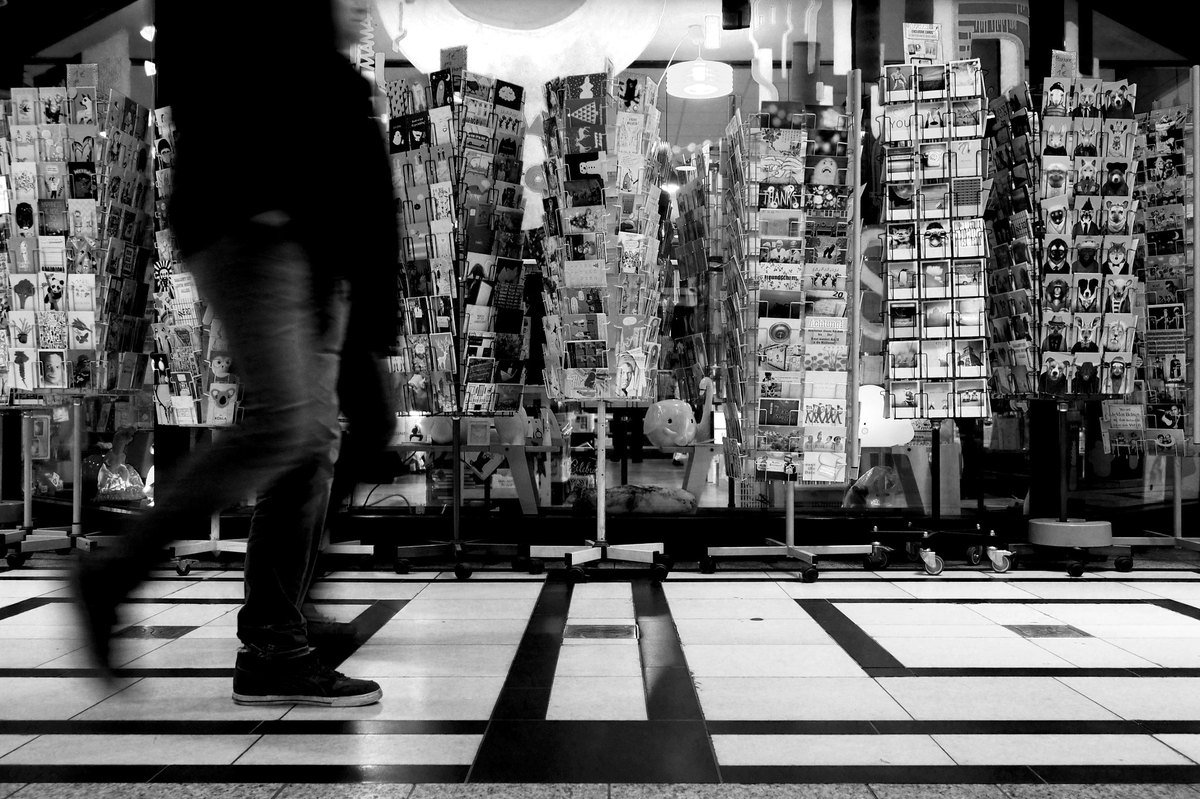 A wall of postcard racks in a shop, with a person walking past in a blur.