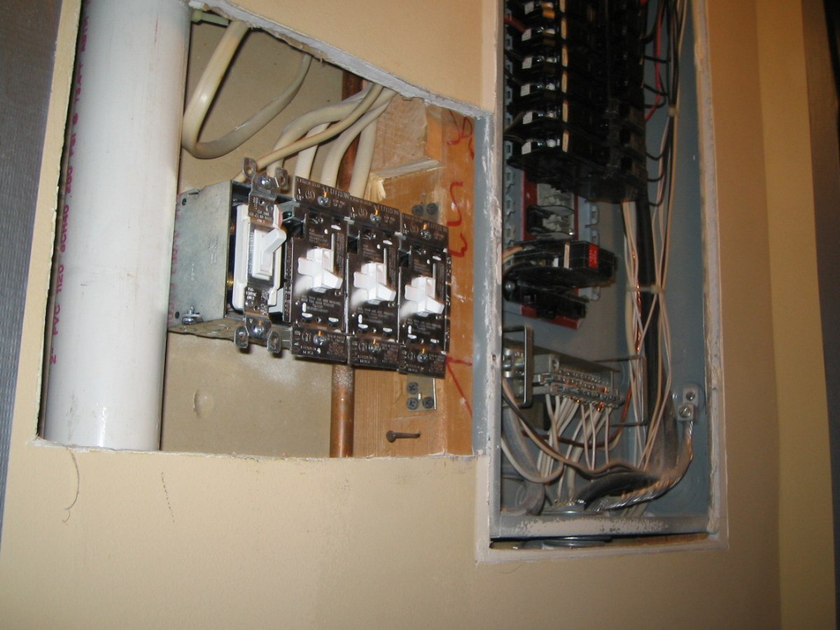 Four wall switches beside an open household breaker panel.