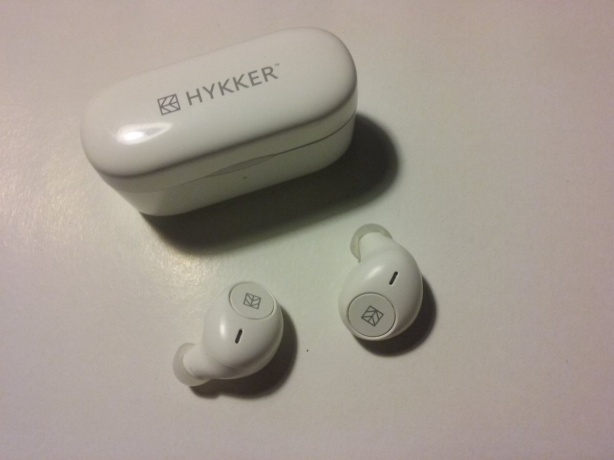 A pair of white wireless earbuds next to their charging case.
