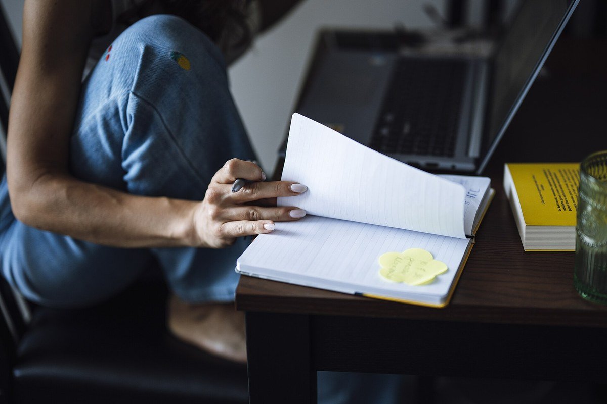 A person writing by hand in an open notebook next to a laptop on a table.
