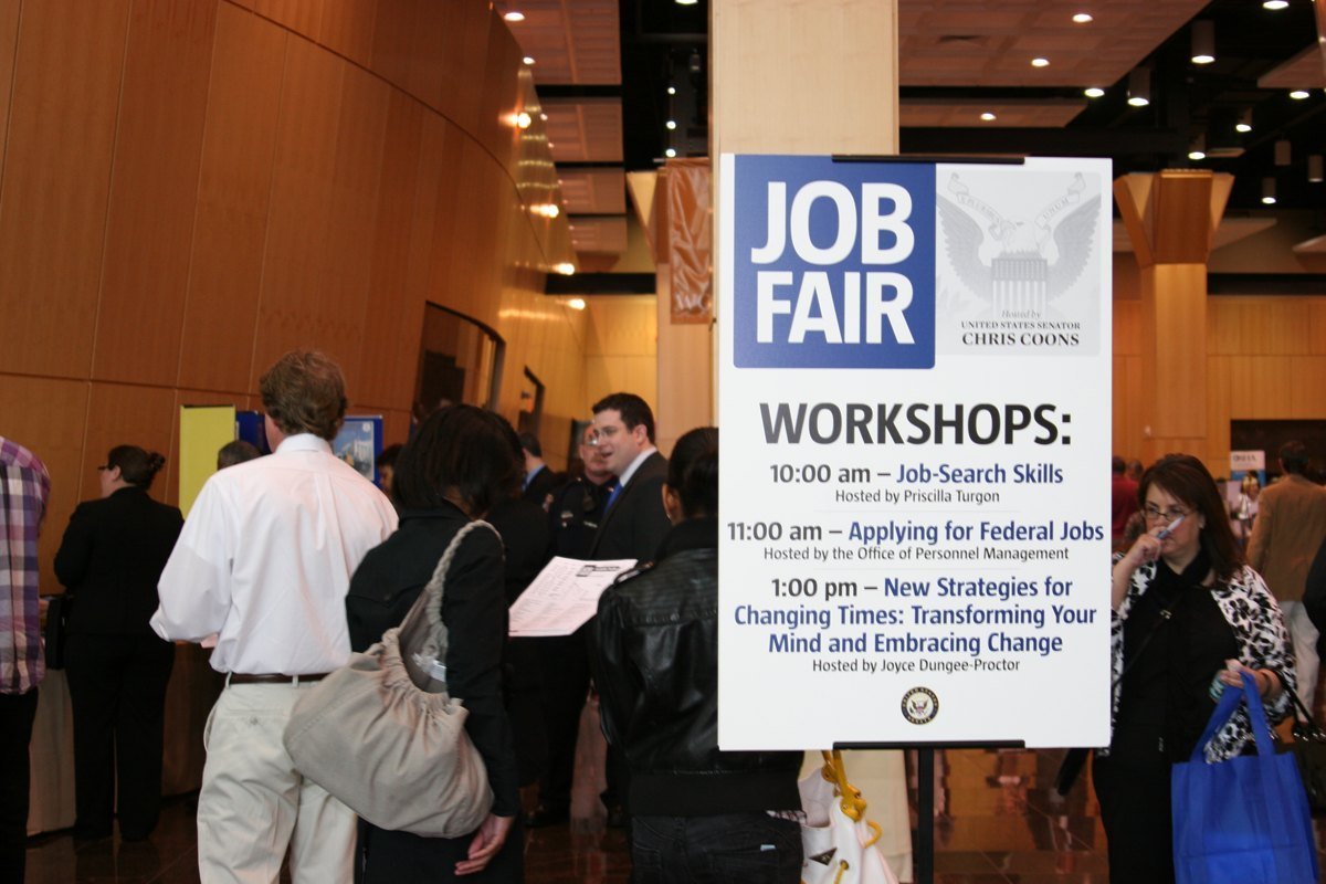 A job fair sign in a crowded convention hall listing workshops on job-search skills and applying for federal jobs