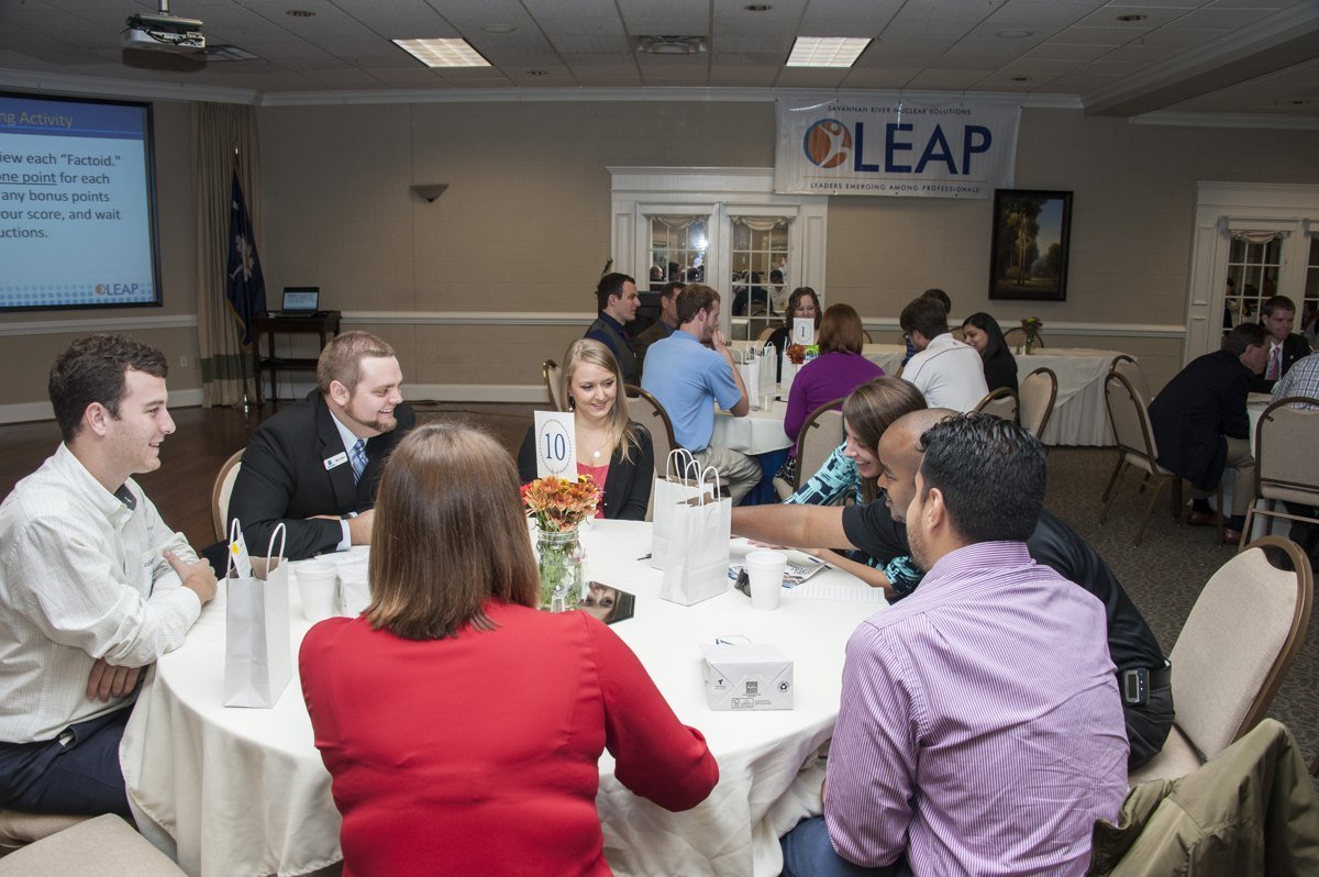 Young professionals talk around round tables at a 2015 networking event in a banquet room, with a LEAP banner on the wall