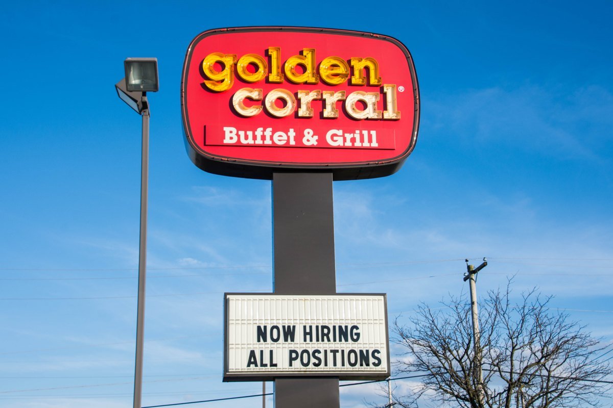 A tall red Golden Corral Buffet and Grill sign against a blue sky, with a white letter board below it that reads Now Hiring All Positions.