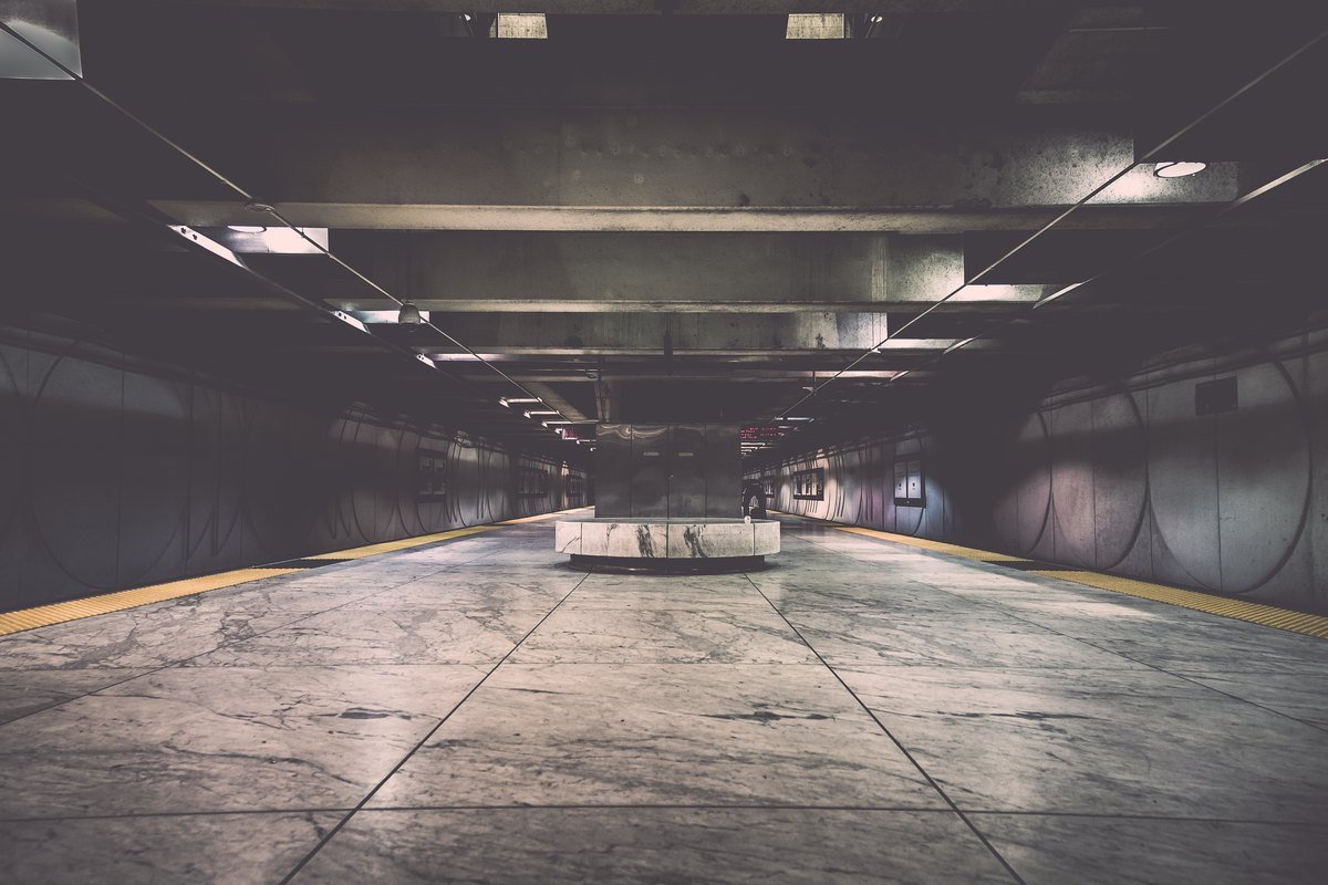 An empty underground BART platform at Embarcadero station in San Francisco, with marble floor tiles and curved wall panels.