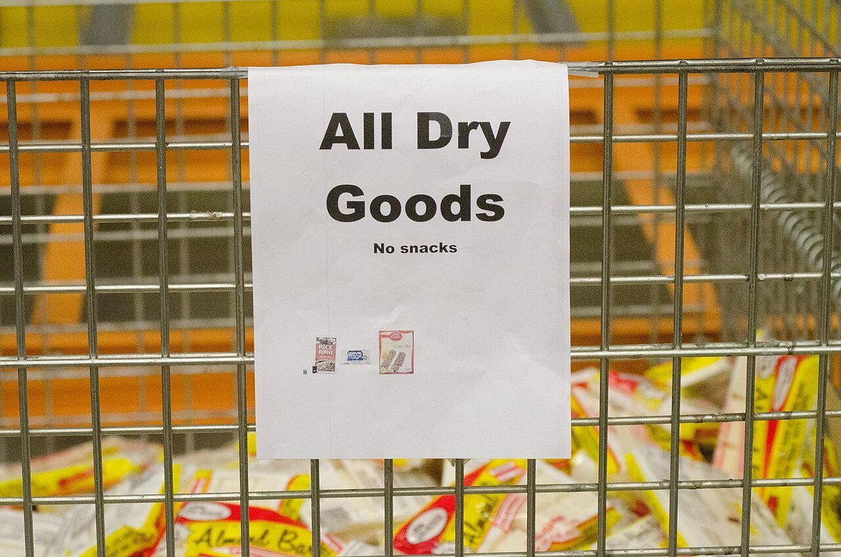 A wire sorting bin at a food bank with a hand-written sign reading All Dry Goods, No snacks