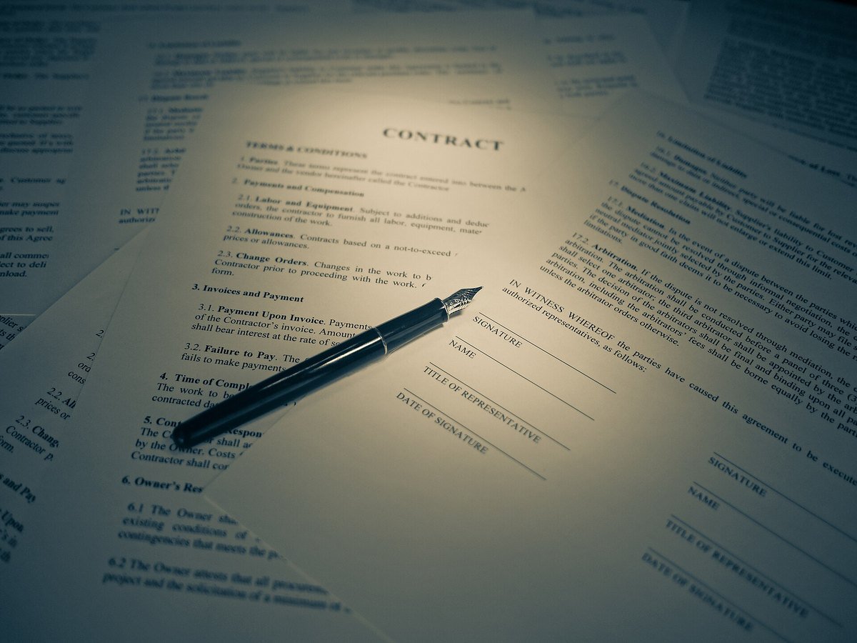 Printed contract pages fanned out under a warm light, with a fountain pen lying across a signature line