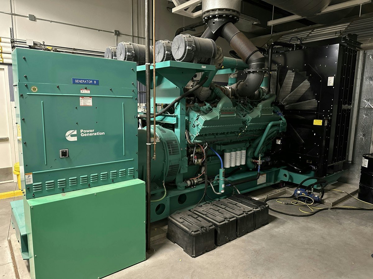 A large green diesel generator unit with an exhaust stack inside an indoor equipment room, used as backup power for a hospital data center.