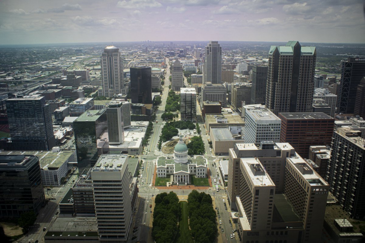 View of downtown St. Louis from the top of the Gateway Arch, with office towers on both sides of a long green mall leading to a domed courthouse.