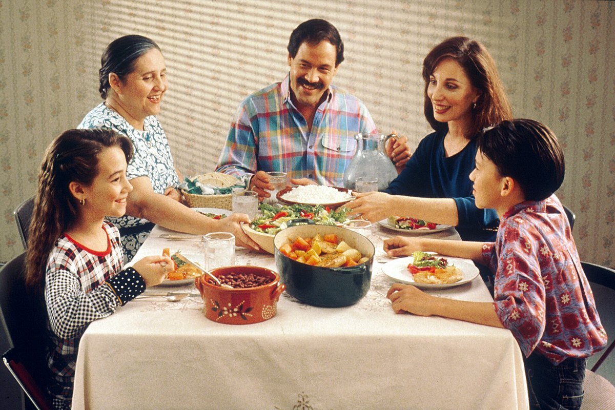 A family of five shares a meal at a dinner table with a white tablecloth