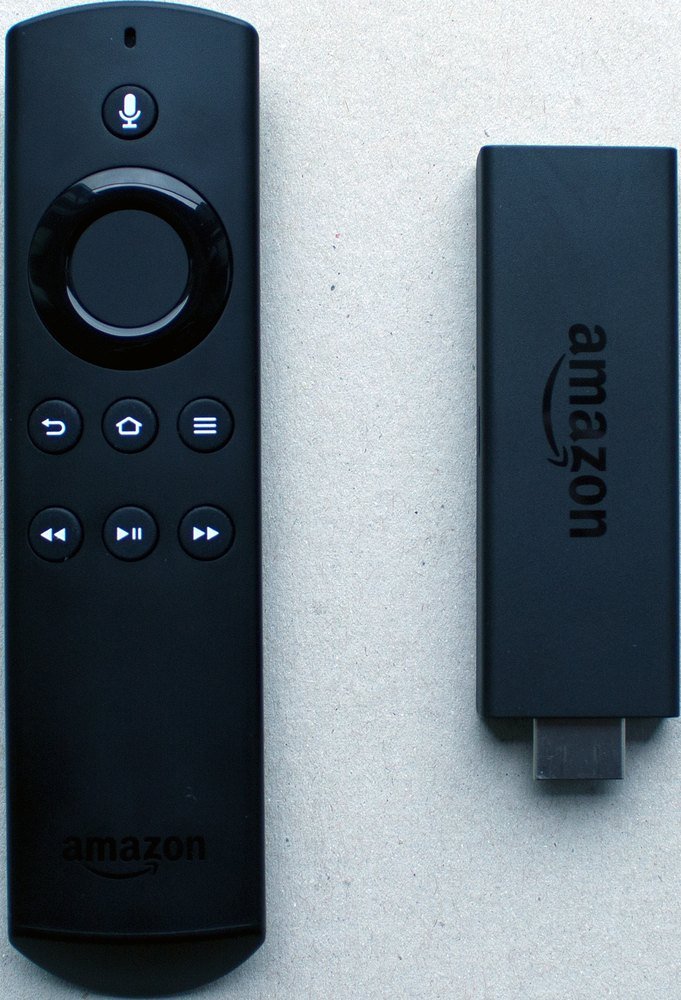 An older Amazon Fire TV Stick lying next to its black voice remote with a microphone button at the top
