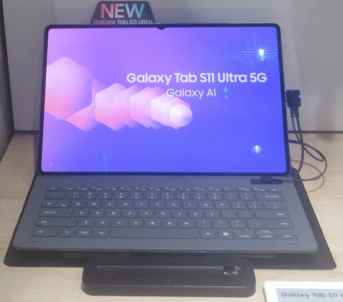 A Samsung Galaxy Tab S11 Ultra on a store display stand with a keyboard cover, its screen showing Galaxy AI