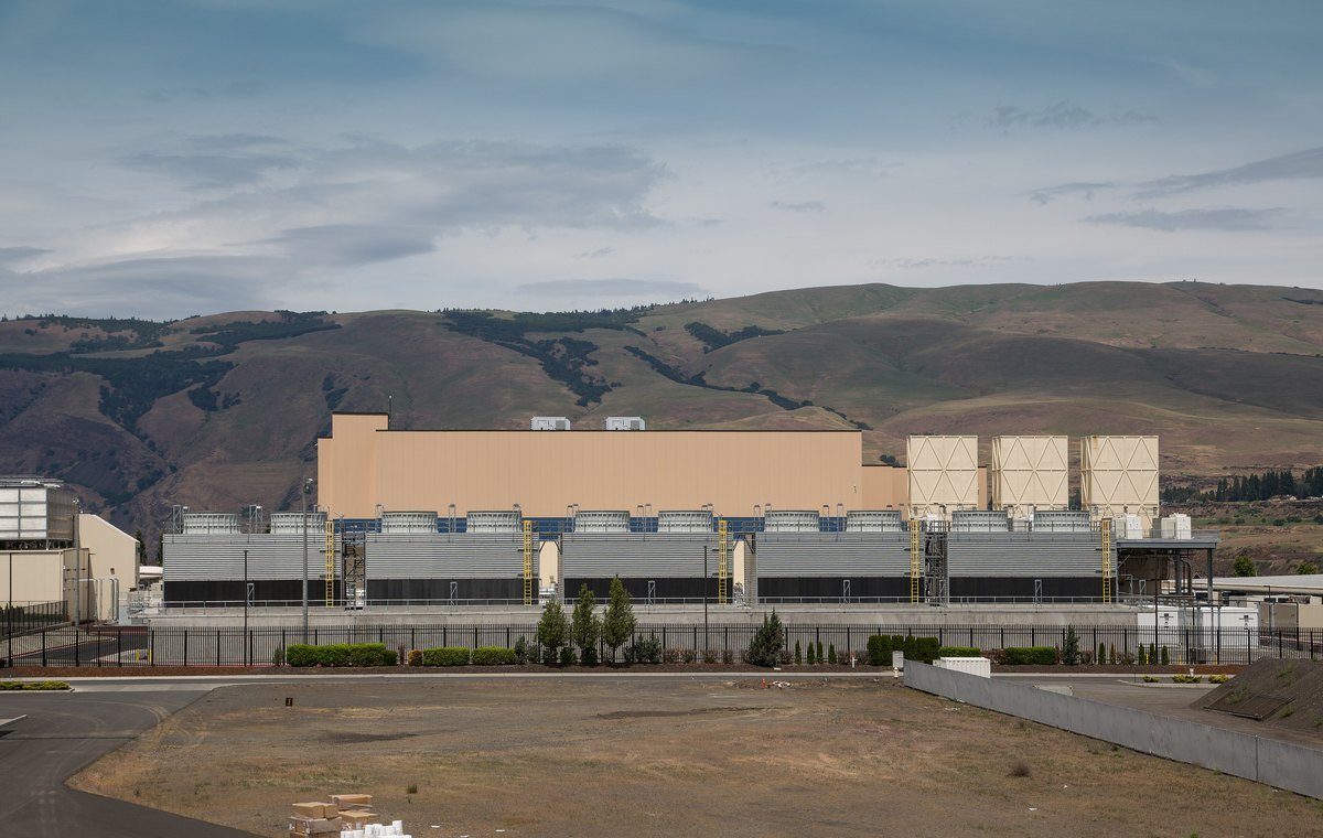 Google's data center in The Dalles, Oregon, a long low building with rows of cooling units in front of brown hills along the Columbia River gorge.