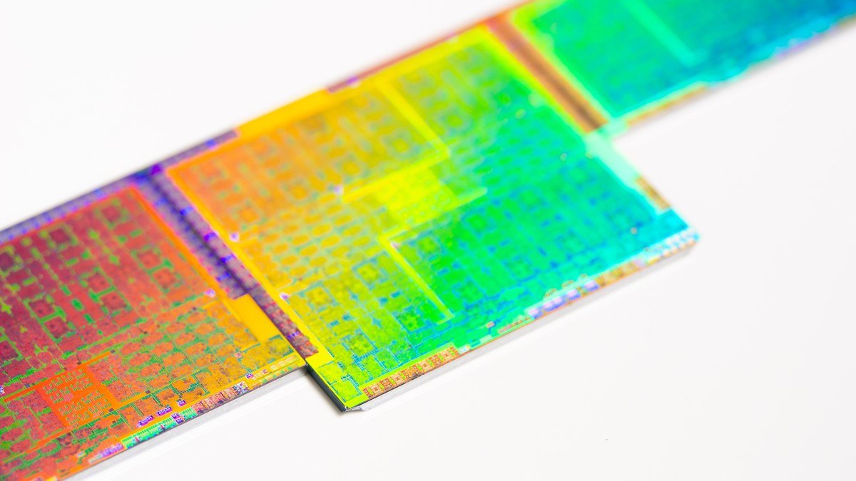 Close-up of three bare graphics processor silicon dies stacked at an angle, their surfaces showing colorful iridescent circuit patterns on a white background.
