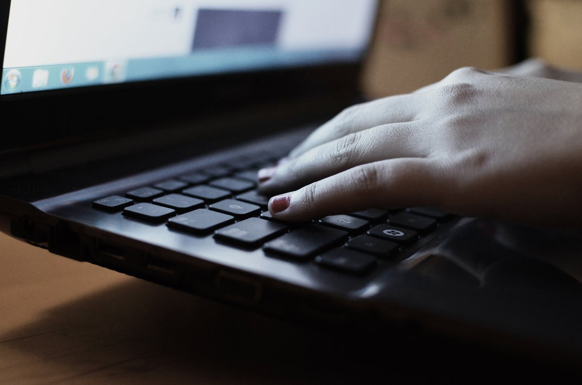 Close-up of a hand resting on a black laptop keyboard in low light, a browser window open on the screen.