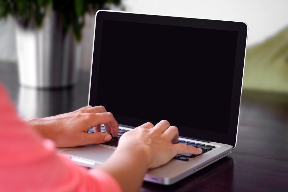 Two hands typing on a silver laptop keyboard at a dark wooden table, screen dark.