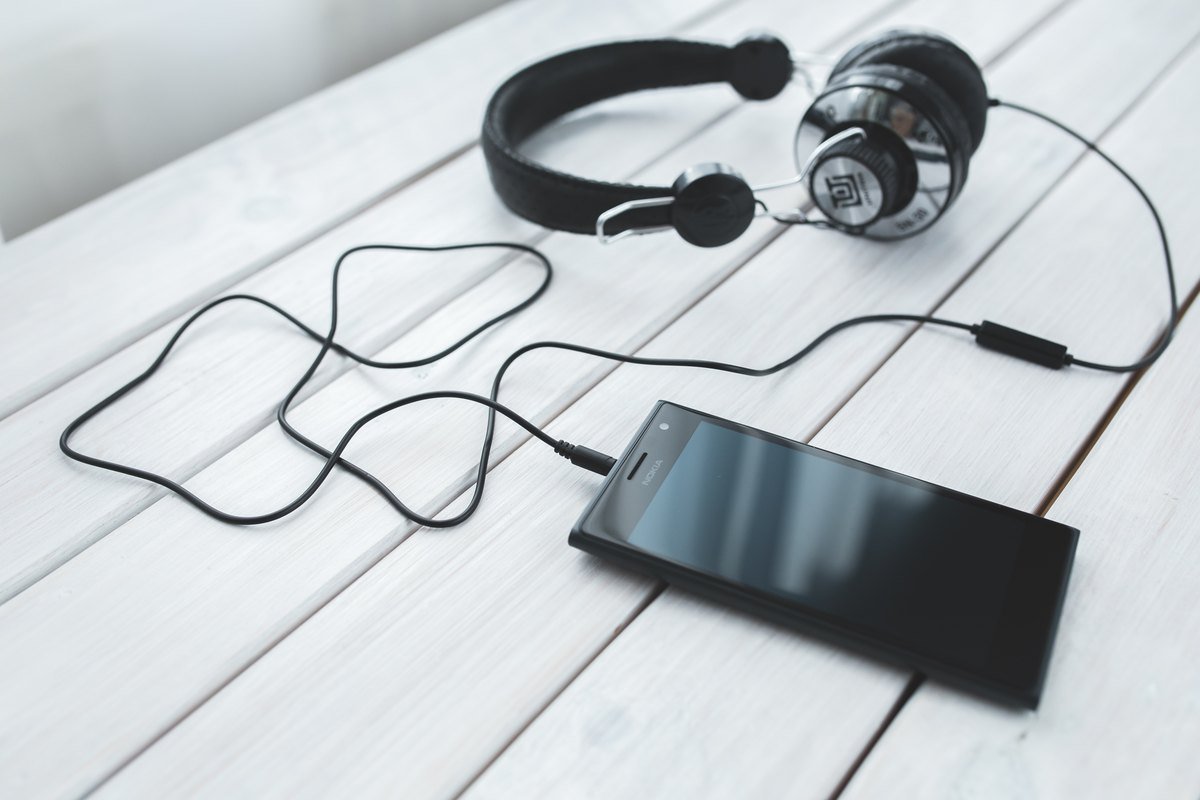Wired headphones plugged into a black smartphone lying on a white wooden table