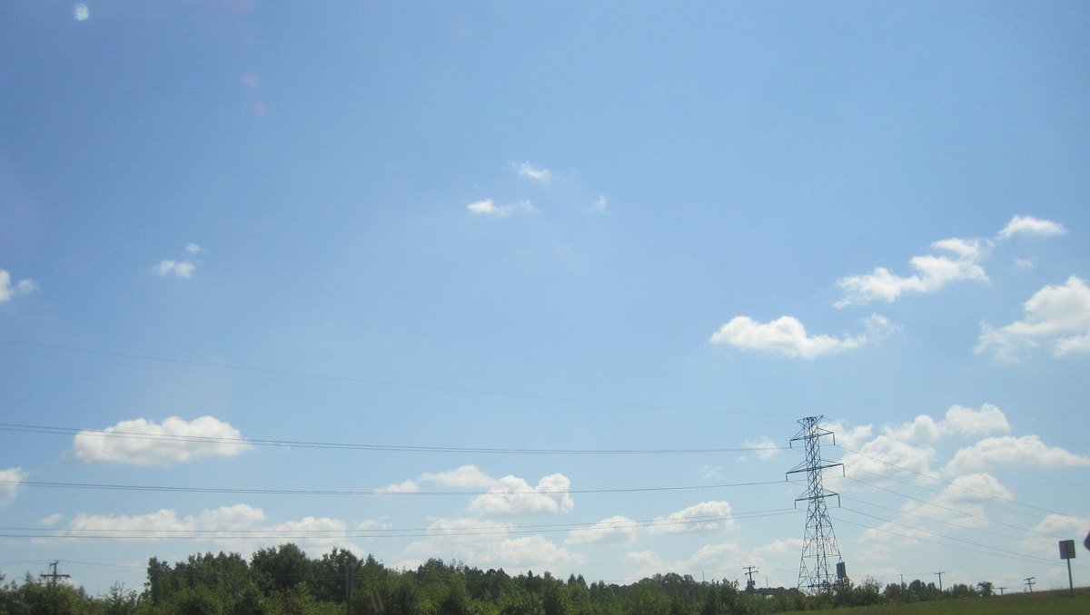 High-voltage transmission lines on tall steel towers crossing over a highway in Virginia under a partly cloudy sky.