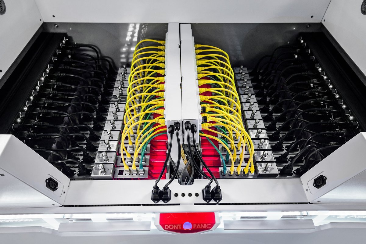 Top-down view into an open immersion cooling tank holding rows of server boards submerged in clear fluid, with yellow and black network cables attached.