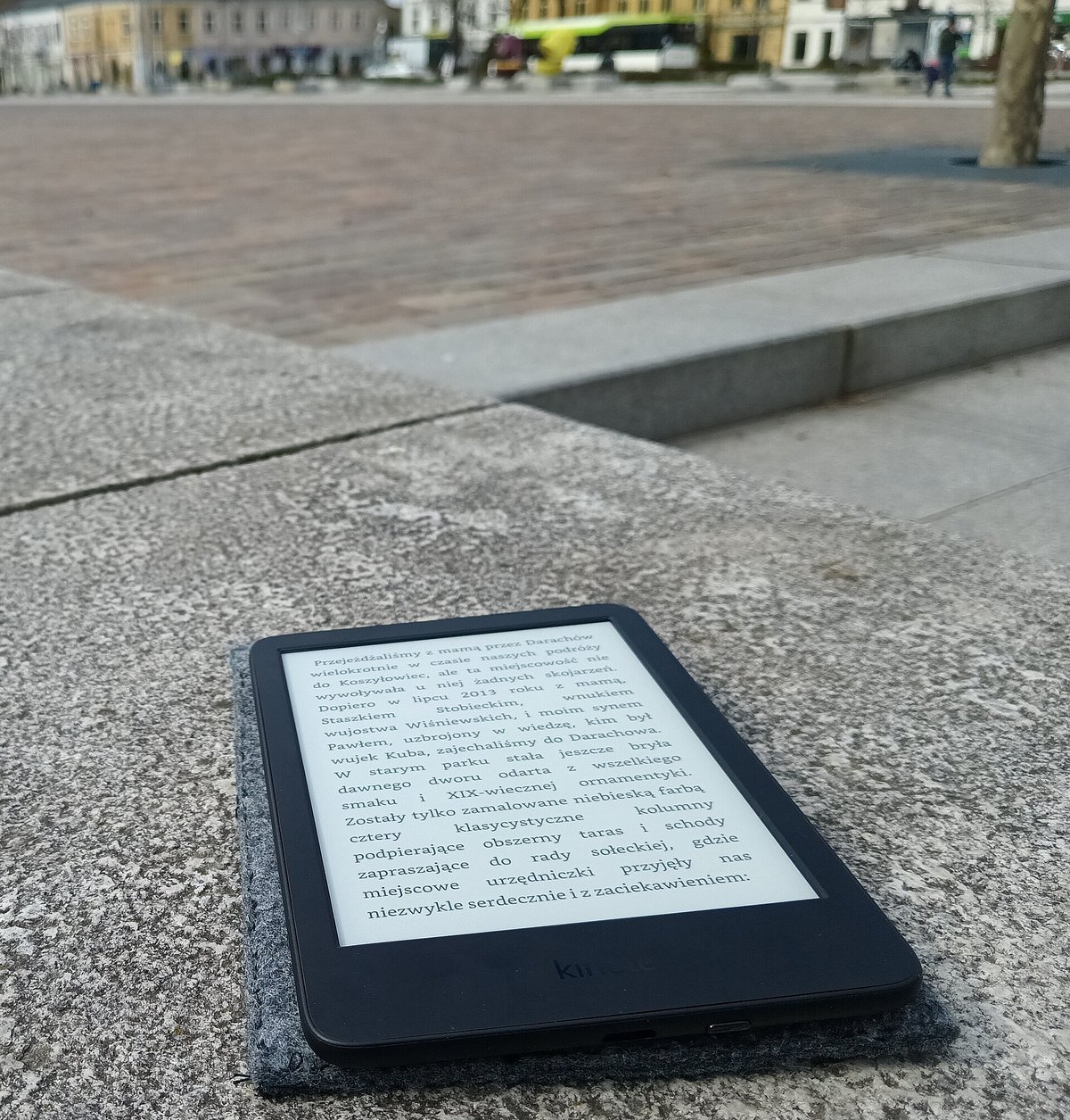A black Kindle Paperwhite e-reader lying on a stone ledge, showing a page of text