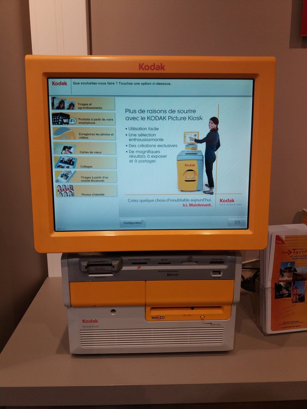 An orange Kodak Picture Kiosk with a touch screen and print slot inside a shop