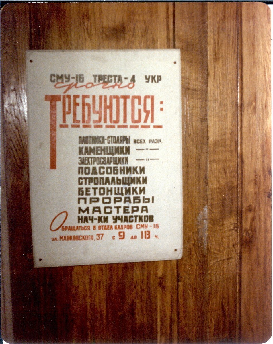 A printed Russian help wanted poster pinned to a wooden door, listing carpenters, bricklayers, electric welders, laborers and other building trades in large red and black letters.