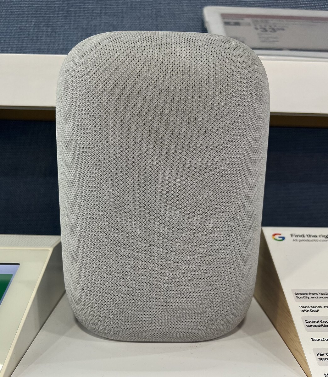 A light gray Google Nest Audio speaker standing on a white store display shelf