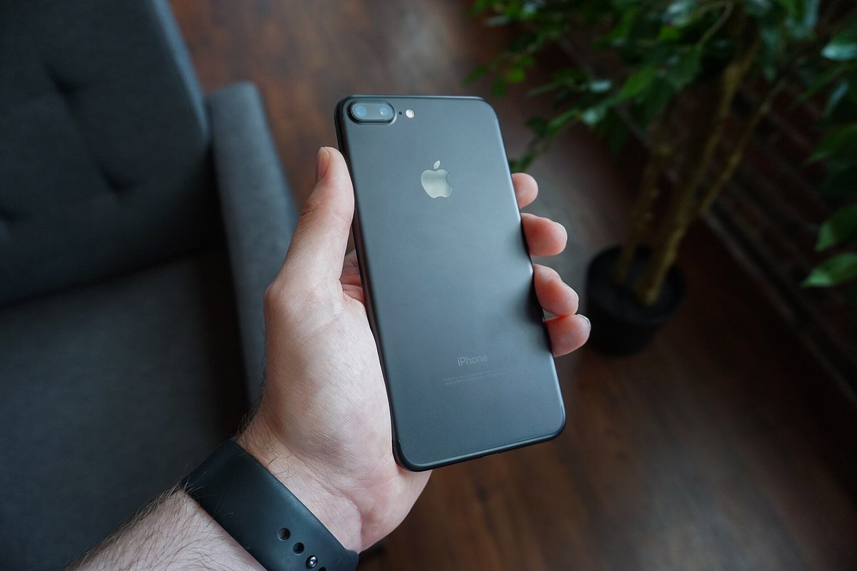 A hand holding a black smartphone with its screen dark, against a blurred background
