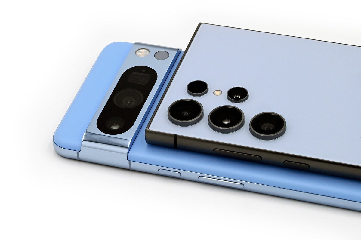 A light blue Google Pixel 8 Pro lying beside a Samsung Galaxy S24 Ultra, both seen from the back with their camera modules