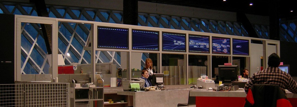 The reference desk and public computer area of a large public library, with staff at the desk and screens on the wall
