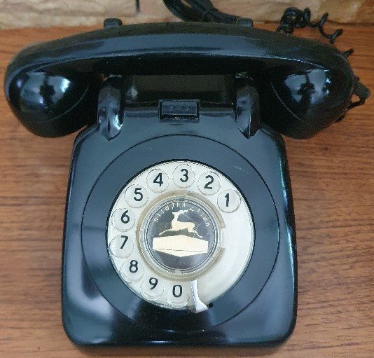 A black rotary dial telephone on a wooden table