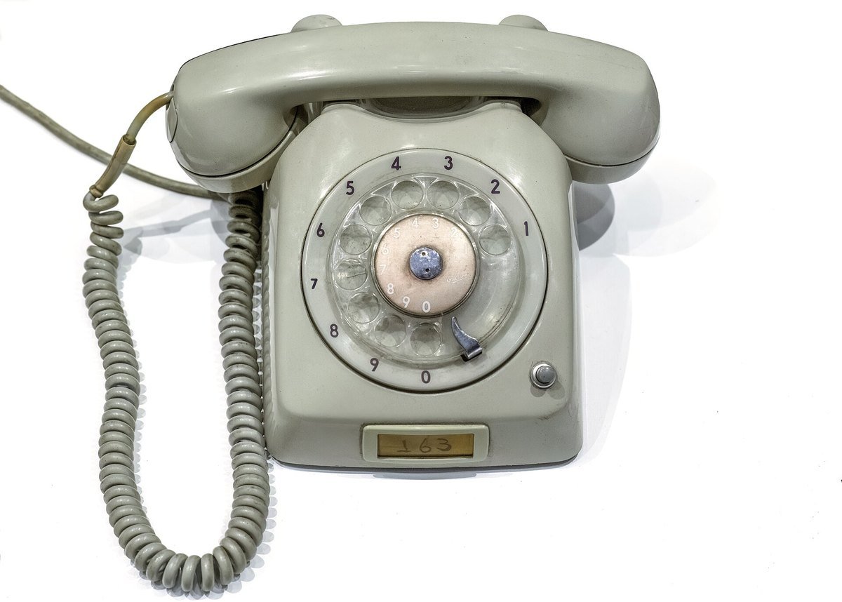A gray rotary dial desk telephone with a coiled cord on a white background