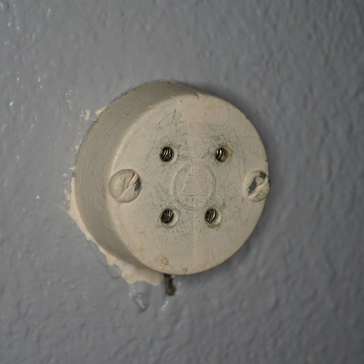 A round, cream-colored four-screw telephone jack on a painted wall