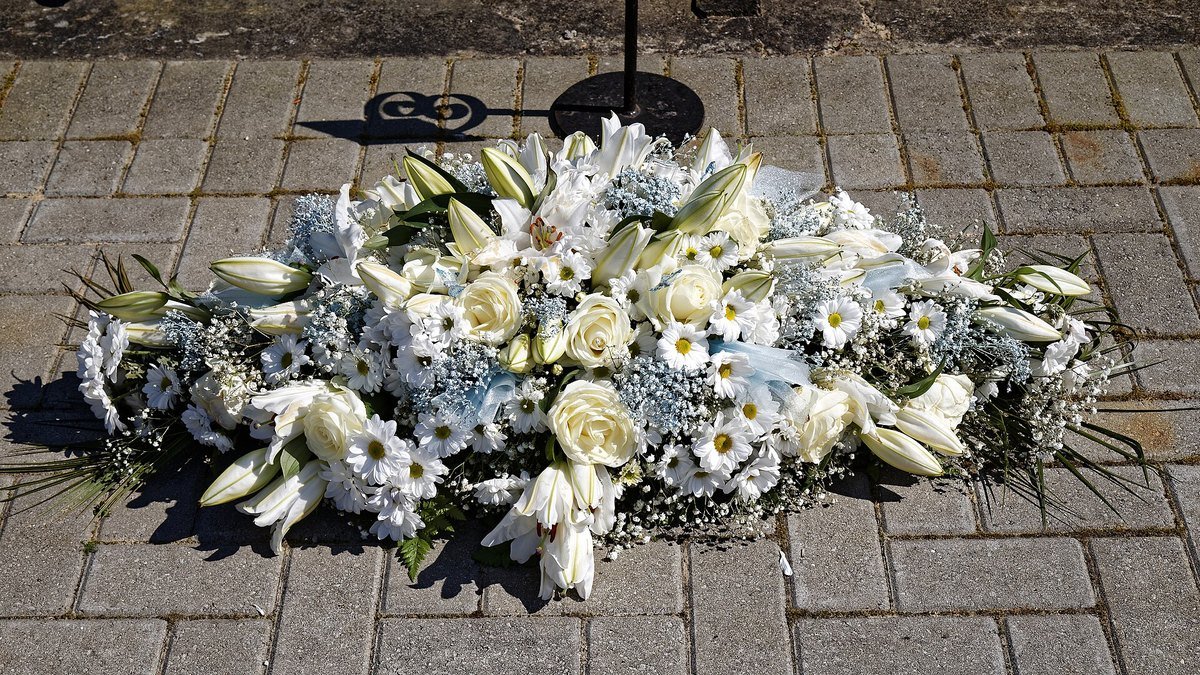 A large spray of white lilies, roses and daisies lies on paving stones at a cemetery