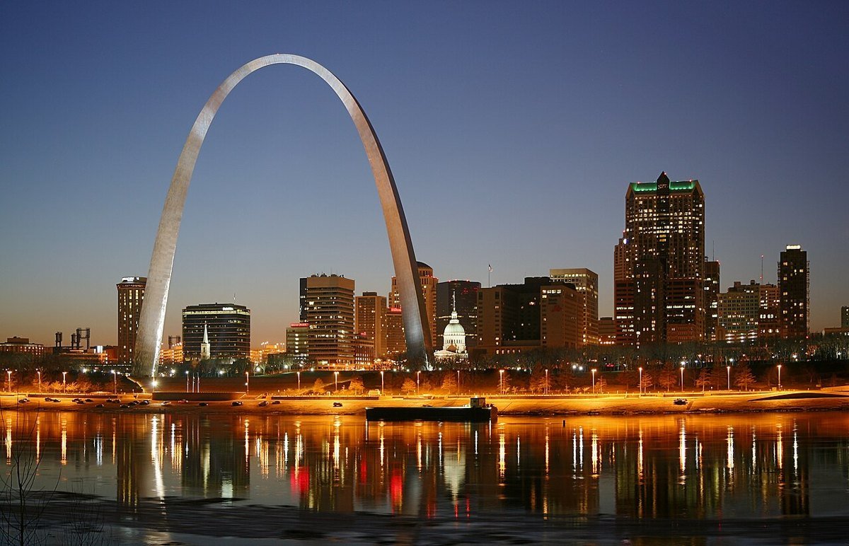 The Gateway Arch and downtown St. Louis at dusk, with city lights reflected in the Mississippi River.