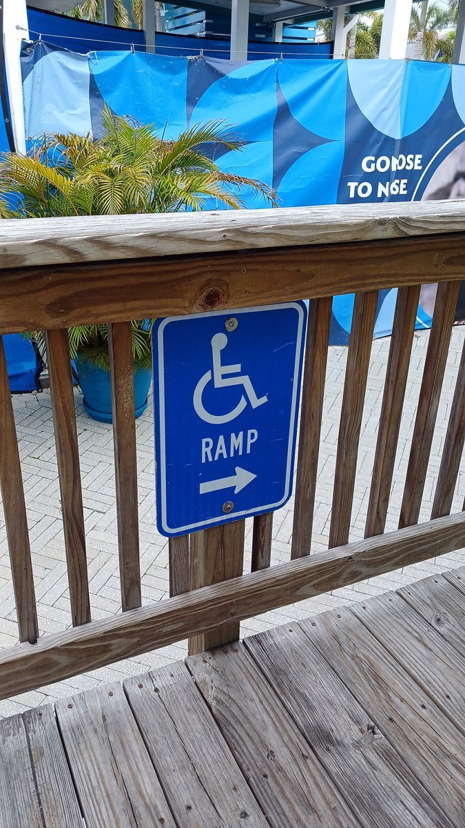 Blue wheelchair ramp sign with the international symbol of access and an arrow, mounted on a wooden railing at the Florida Aquarium in Tampa.
